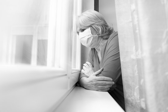 Sad Senior Woman Looking Outside Her Window With Mask On Face, Coronavirus