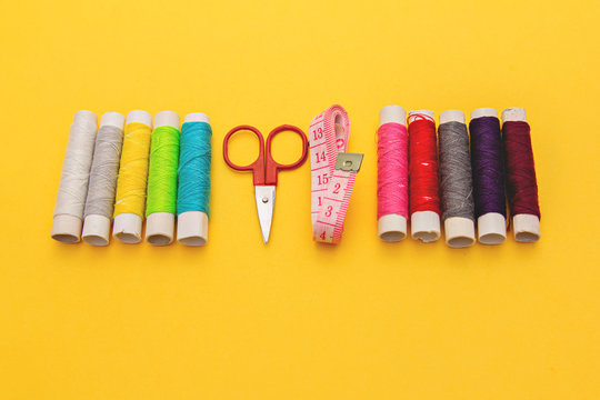 Thread, needles, scissors and meter on yellow background. tailoring set. sewing kit multi-colored.