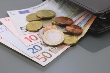 Euros, various bills and coins inside a wallet, close-up on dark background. Cash money