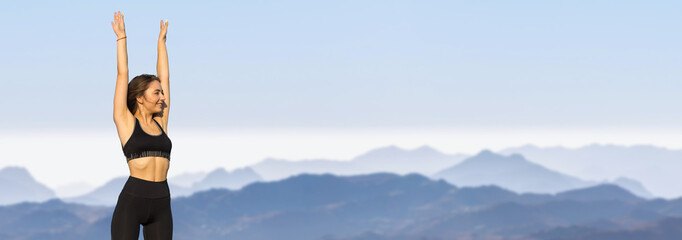 A thin athletic girl takes a break between classes on the background of mountains in the early morning, enjoys silence and freedom.