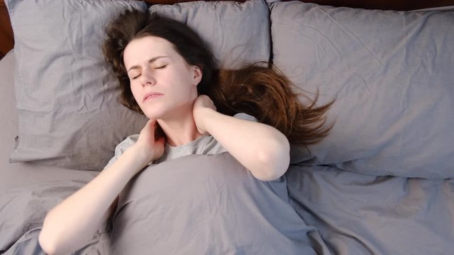 Top close up view upset young woman lying in bed in morning feels pain in neck after night sleep, awaken having painful sudden ache or stiffness, incorrect posture during sleep. Fibromyalgia concept