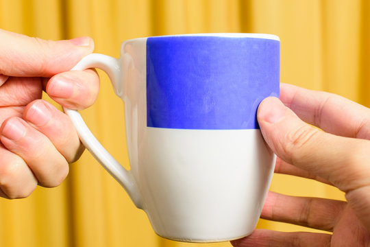 Hand Holding A Blue Cup . Hand Passing A Cup Of Coffee To Another Person. Background Yellow. Full Color.