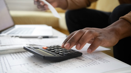 Close up black man hand using calculator and laptop for calculating finance. African american...