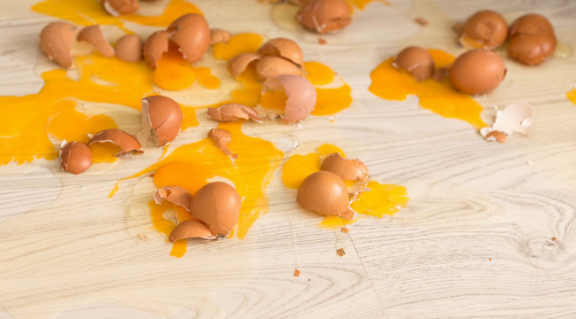 A dozen broken eggs on a wooden floor. Broken egg tray. Culinary incident. Trouble