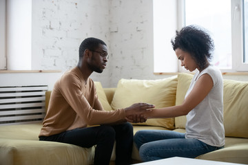 Fototapeta premium Care african american man comforting upset depressed woman holding wife hand for supporting frustrated disappointed girlfriend having life problem, showing love and support.