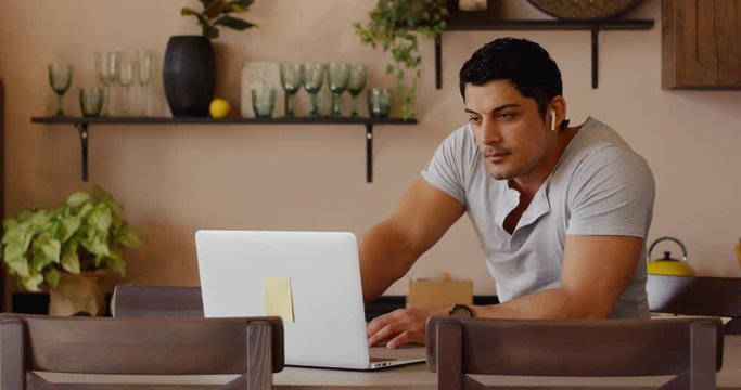 Hispanic male having a conversation during video call with colleagues, kitchen background. Quarantine working, stay home, coronavirus pandemic.