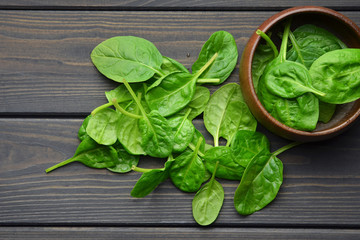 Spinach leaves in wooden bowl on dark wooden table background. Healthy vegan food trend. Vegan lifestyle concept. Top view.