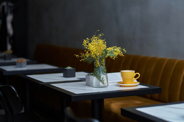 mimosa in a vase and coffee in a yellow cup on a table in a cafe or restaurant