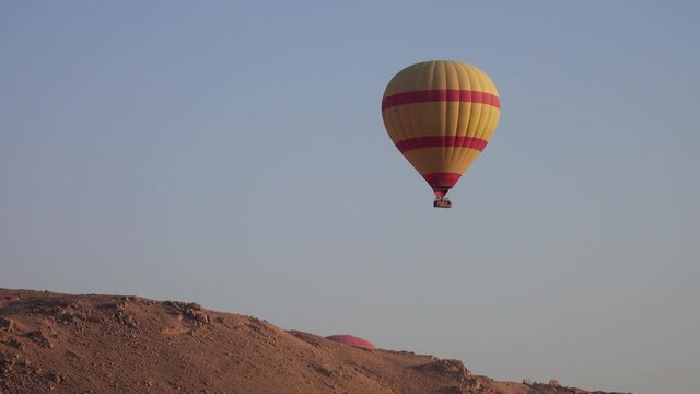 Yellow and red hot air baloon flying in blue sky over mountain, 4k