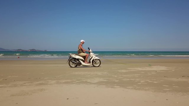 a flying camera takes pictures of a man riding a motorbike in the sand on the beach. Nha Trang Vietnam