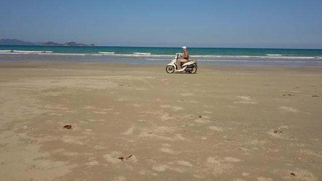 a flying camera takes pictures of a man riding a motorbike in the sand on the beach. Nha Trang Vietnam