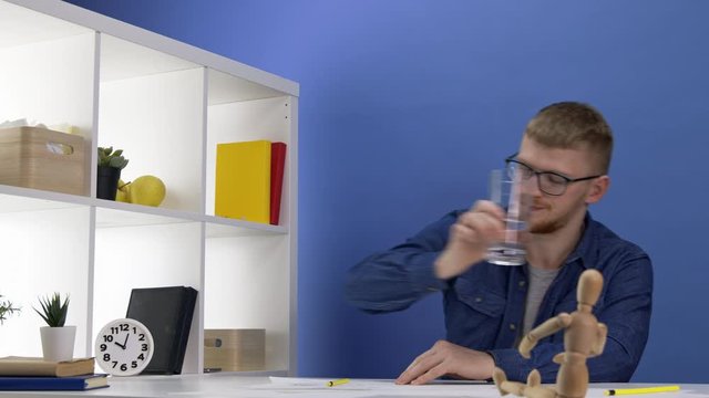 Young attractive painter, illustrator or designer in casual clothes and glasses sitting at desk at home office, working on layout, making pencil sketch. Dummy in the foreground, creative work concept