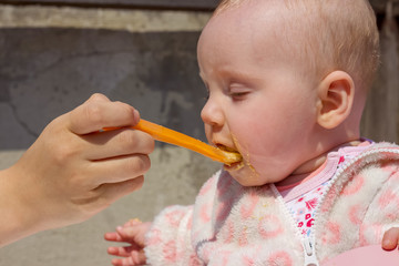 Mom feeding her little cute blonde baby girl with her baby's favorite food and baby's mouth is dirty,supplementary food