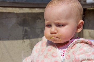 Little adorable blonde baby girl stand,this cute baby looking to the somewhere and her mouth is dirty also she is sad
