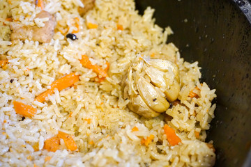 Fragrant friable pilaf, folk traditional dish of Uzbekistan, rice background and carrots, whole cooked head of garlic