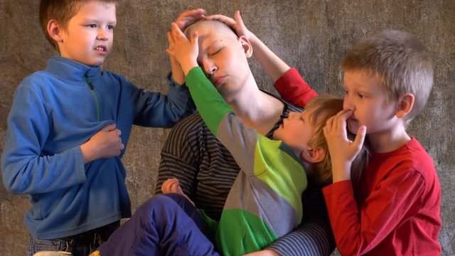 Attractive girl with shaved bald head. Beautiful middle-aged woman with cancer without hair. Children in colorful clothes pat their mother&rsquo;s head and regret after chemotherapy session