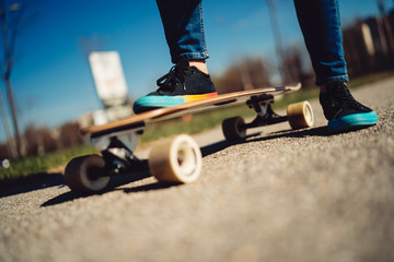 Close up photo of longboard and feet of young girl in sneakers on a road