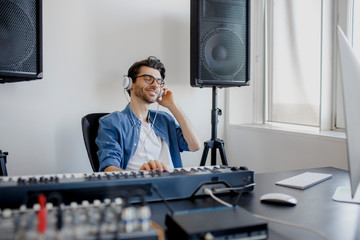 Male music arranger composing song on midi piano and audio equipment in digital recording studio. Man produce electronic soundtrack or track in project at home. - obrazy, fototapety, plakaty