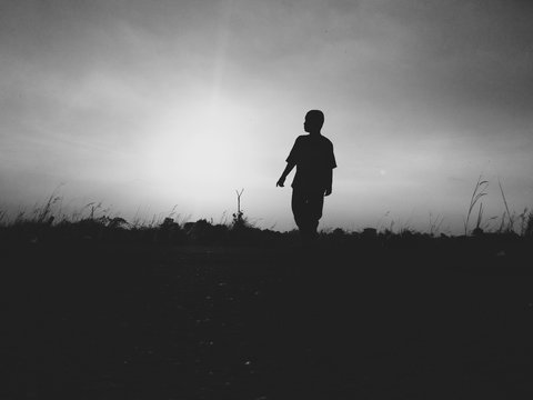 Silhouette Boy Walking On Field Against Sky During Sunset