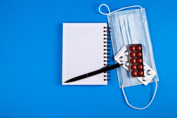 Notebook with tablets and medical mask on a blue background. Top view. Copy space.