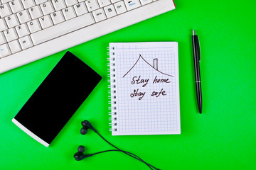 Stay home concept. Keyboard with smartphone, headphones, pen and notebook on a green background. Top view.