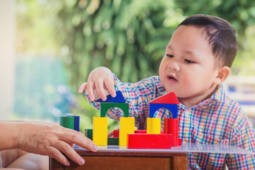Child playing with wooden colorful blocks. Little boy intend to building tower by wooden colorful...