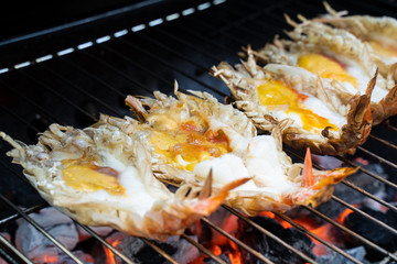 Big prawns, lobsters grilling on barbecue grill coal oven equipment, hot fire below grate . Each have melt yellow creamy delicious fat on head after cooked. Awesome yummy taste. Tasty seafood grilled.