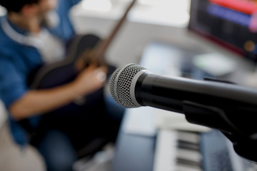 focus on the microphone, blurred background Man plays guitar and produce electronic soundtrack or track in project at home. Male music arranger composing song on midi piano and audio equipment in