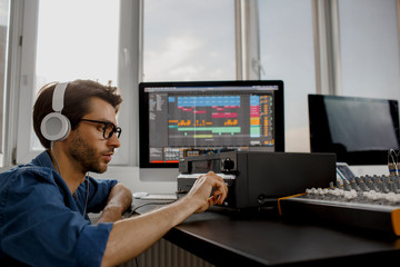 Fototapeta na wymiar Male music arranger works with sound amplifier he is composing song on midi piano and audio equipment in digital recording studio. DJ in broadcasting studio. music, technology and equipment concept.