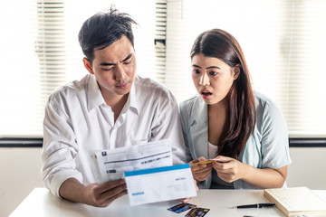 Asian young couple shocked and stressed with bills. Man and woman try to find money to pay credit...