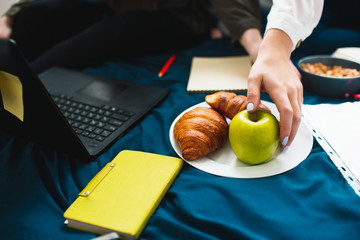 close up plate. There is a croissant green apple and nuts. Girl wants to take. Two red-haired students study at home or prepare for exams. Women doing homework in a dormitory bed near the window.