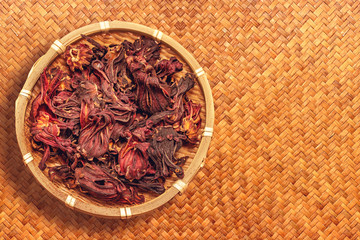 dried roselle flower in wooden bowl on brown woven reed mat background for made herbs tea or rosella Juice