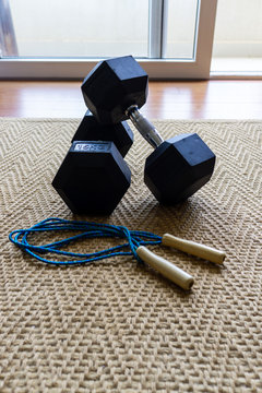 Two Hex dumbbells and a skipping rope stored at on the floor at home