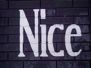 Close Up of Black Brick Wall with Word Nice in Worn White Paint