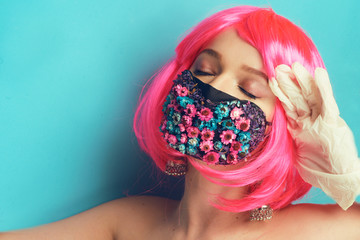 Girl in a mask and gloves, fashion photo. A model with pink hair posing in a studio in a mask of flowers gloves, spring's fashion. Pandemic, coronavirus, spring. Portrait of a girl on a blue back