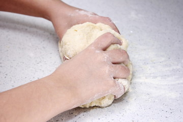 Children's hands knead a piece of dough. The process of kneading the dough