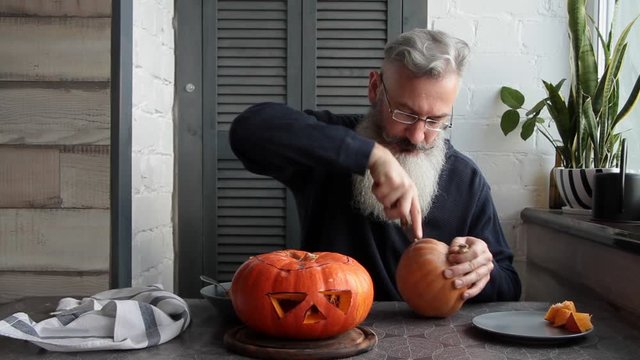 Caucasian mature bearded man makes pumpkin lantern Jack-o-lantern, markup and cut out his eyes and mouth, Halloween concept