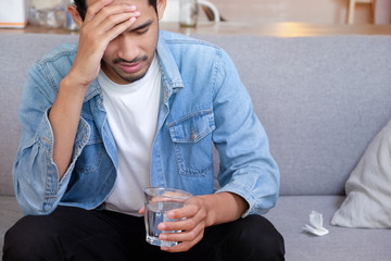 Young man suffering from strong headache or migraine sitting with glass of water
