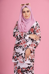 Portraiture of beautiful young Muslim girl wearing batik design dress known as Baju Kurung with hijab. Fashion for dinner, event and Eidul fitri feast.Studio shot with pink background.