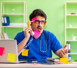 Young doctor sitting in hospital with many conflicting prioritie