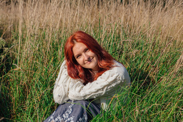 Beautiful happy woman sitting in grass in white sweater