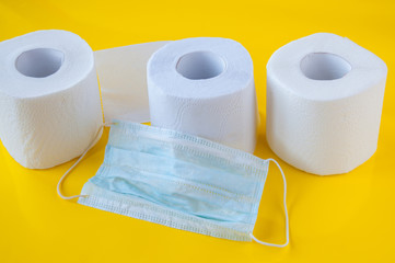 Three rolls of white toilet paper and a medical mask on a yellow background