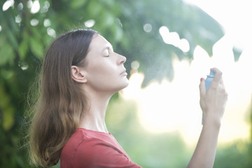 Woman spraying facial mist on her face, summertime skincare concept