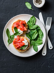 Potato cakes with smoked salmon, sour cream and spinach on a dark background, top view. Delicious snack, tapas, brunch