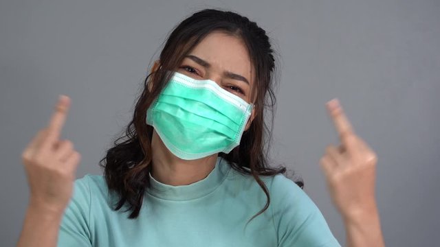 woman in a medical mask(surgical mask) with middle finger fuck sign hand gesture, coronavirus protection