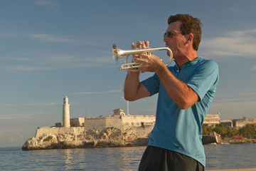 A trumpet player playing music in front of Castillo del Morro, El Morro Fort, across the Havana...