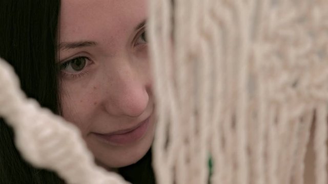 woman weaves macrame on a stick.