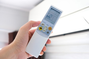 Man's hand using remote control open The air conditioner is cooled to 25 degrees Celsius in his bedroom. Health concepts and energy savings
