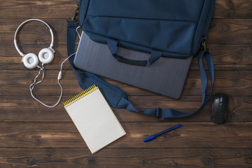 Headphones, Notepad, mouse and laptop in a bag on a wooden background.
