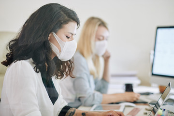 Side view of serious businesswoman sitting next to colleague and working on laptop in office